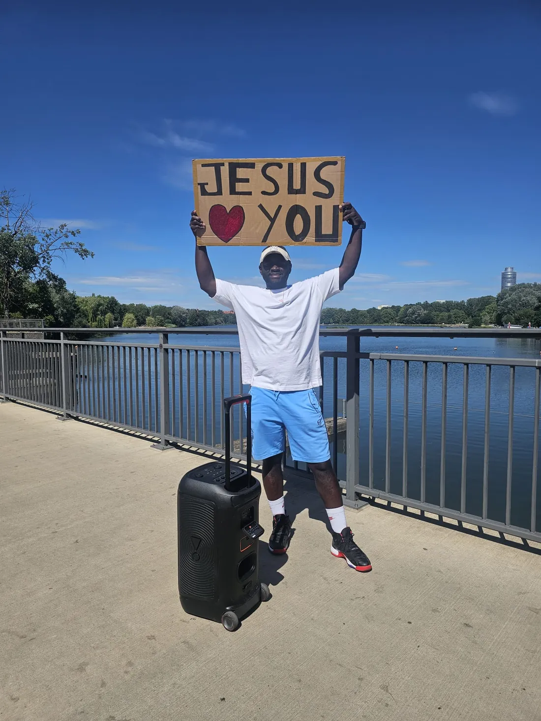 Leo Sokeng mit einem Schild „Jesus loves you“ an einer Uferpromenade