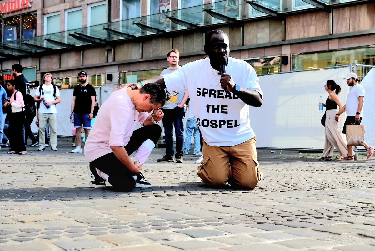 Leo Sokeng betet kniend mit einem Menschen auf der Straße
